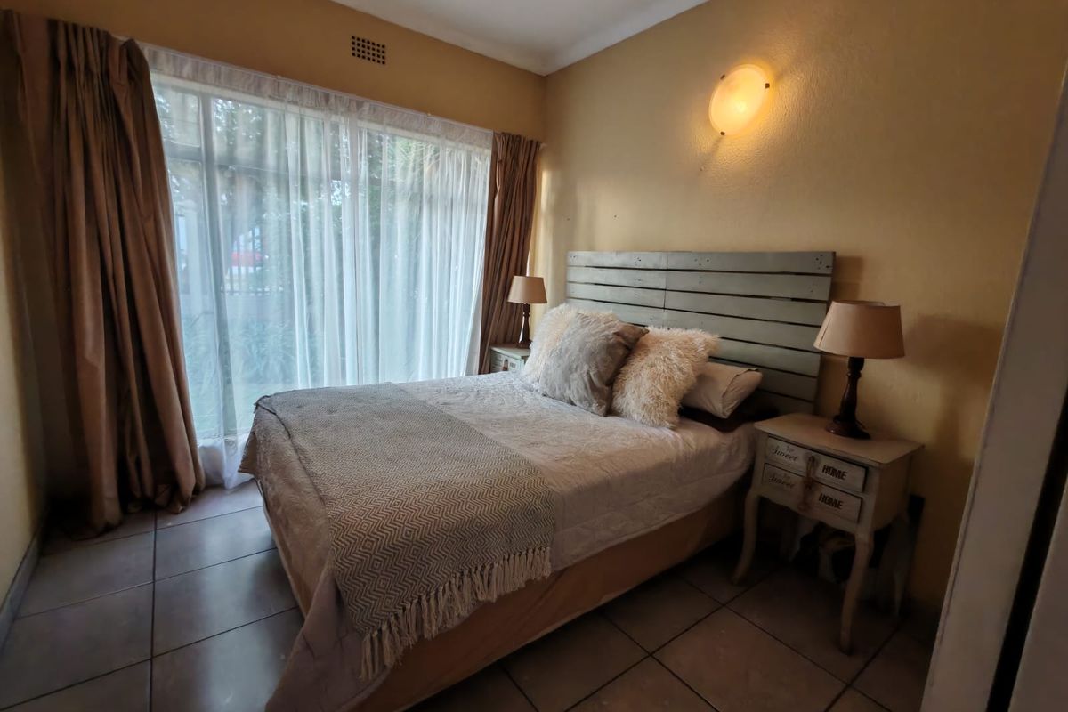A cozy bedroom featuring tiled flooring, a large window with curtains, and a wall-mounted light fixture.
