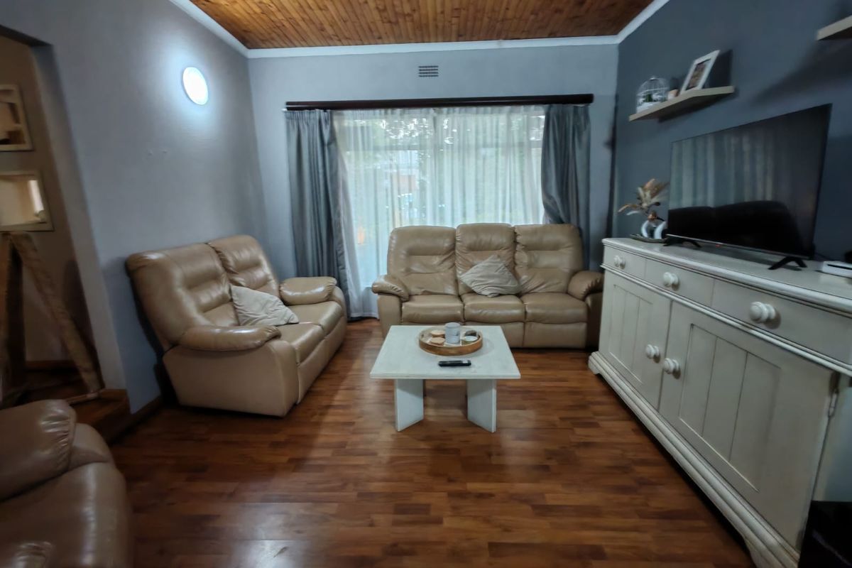 A comfortable living room featuring warm timber ceiling paneling, laminate flooring, and a large sliding glass door providing natural light.