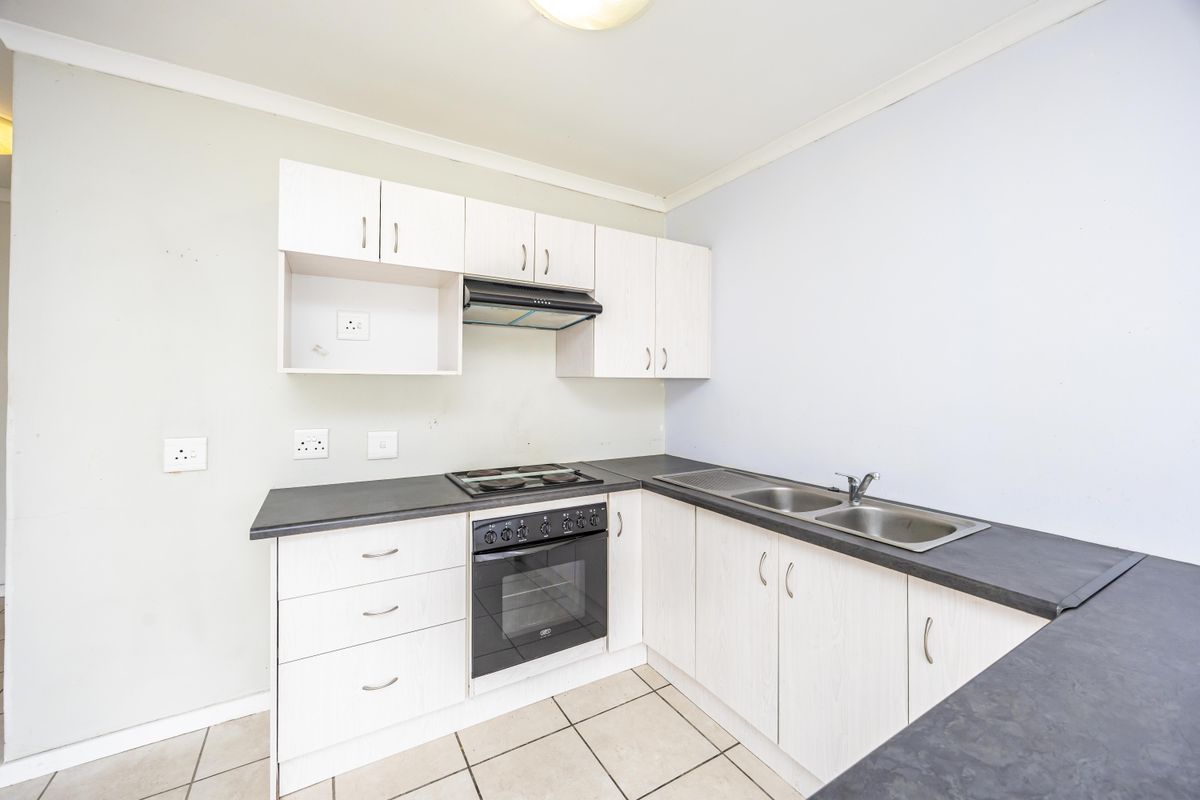A functional kitchen featuring light-toned built-in cabinetry, dark laminate countertops, a stainless steel double sink, and a built-in oven with an electric hob.