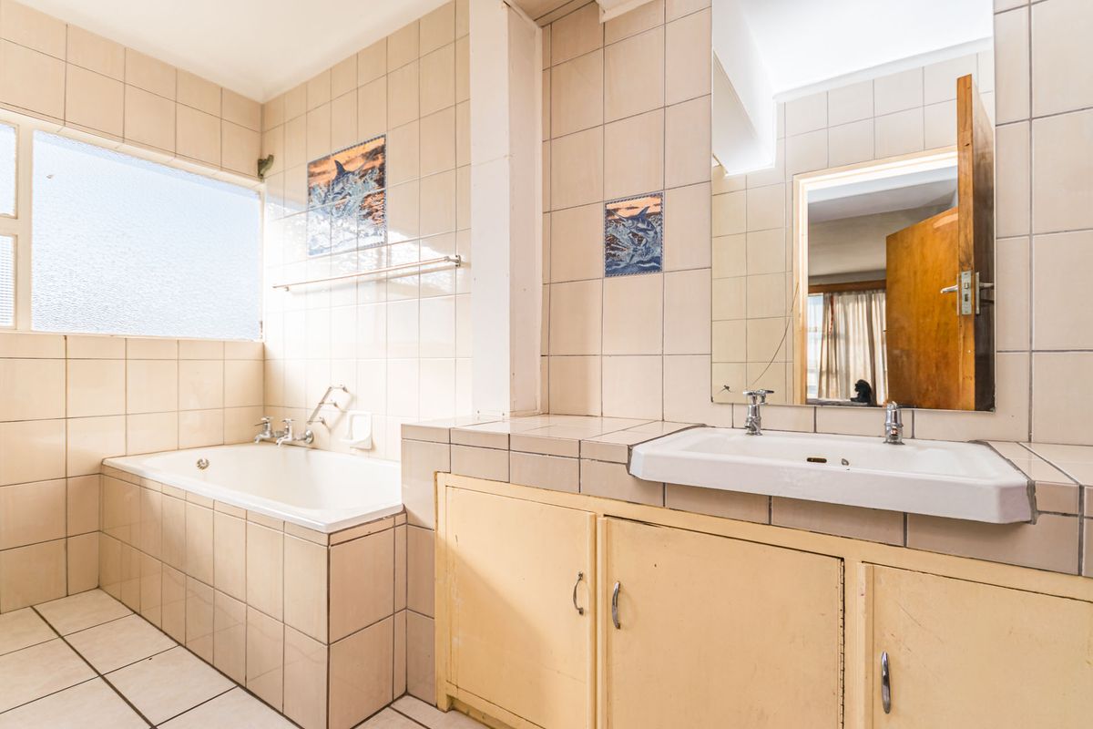 A dated bathroom featuring a built-in bathtub, tiled vanity with basin, and wall-mounted mirror, offering potential for a modern renovation.