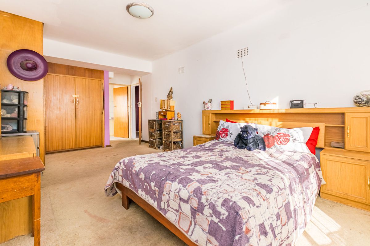 A spacious bedroom featuring built-in wooden cupboards and a matching integrated headboard, offering a functional layout with carpeted flooring throughout.