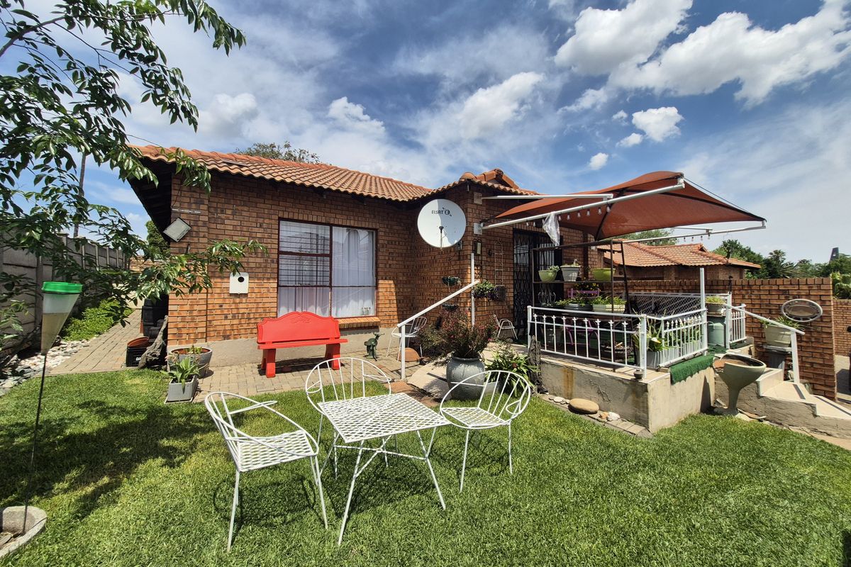 A rear view of a brick townhouse featuring a paved patio area, a small lawn, and a retractable awning over the outdoor space.