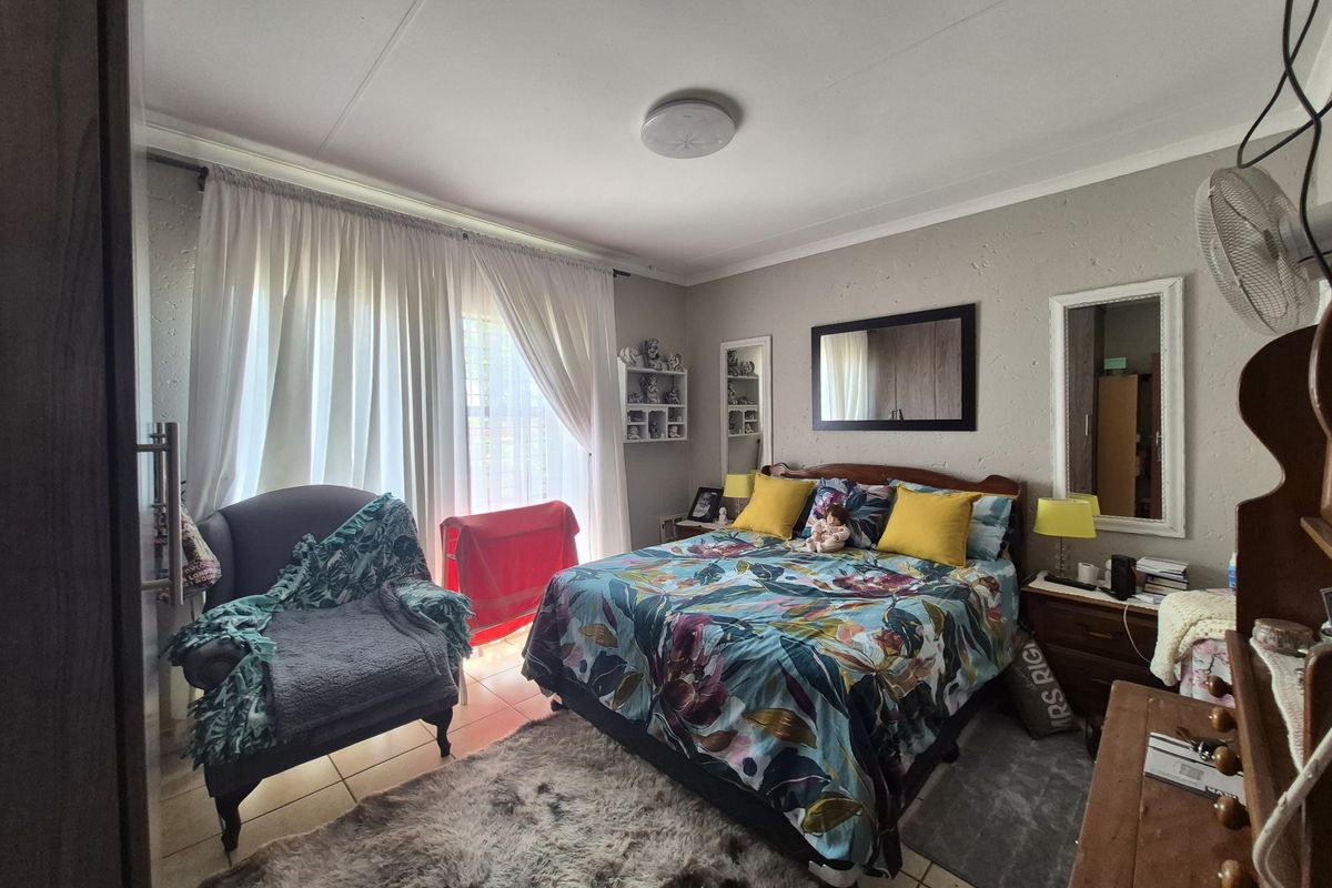 A bedroom featuring tiled flooring, built-in wall shelving, and large windows with curtain tracks, providing a functional and comfortable living space.