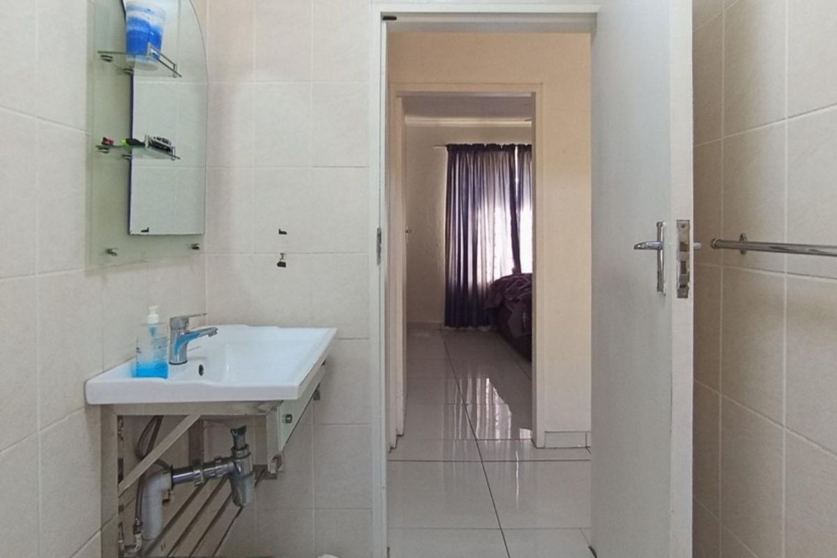 A functional bathroom featuring a wall-mounted basin, tiled surfaces, and a towel rail, with a view leading into an adjacent bedroom.