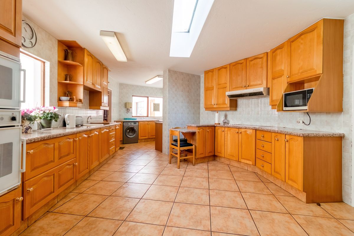 Spacious kitchen featuring warm wood cabinetry, granite countertops, a skylight for natural light, and integrated appliances with tiled flooring throughout.