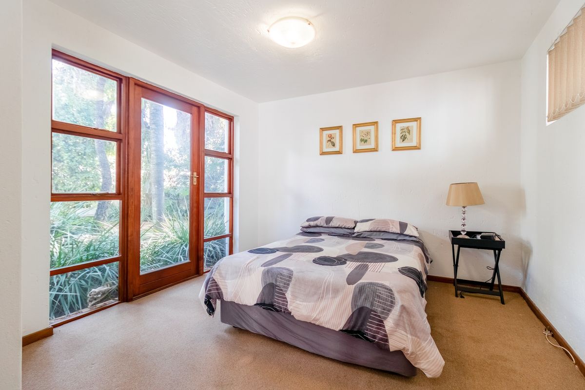 A bright bedroom featuring carpeted flooring and large wooden-framed glass doors providing direct access to the garden area.
