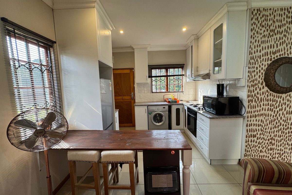 A functional kitchen featuring white cabinetry, granite countertops, built-in oven and hob, and tiled flooring, with an integrated laundry area.