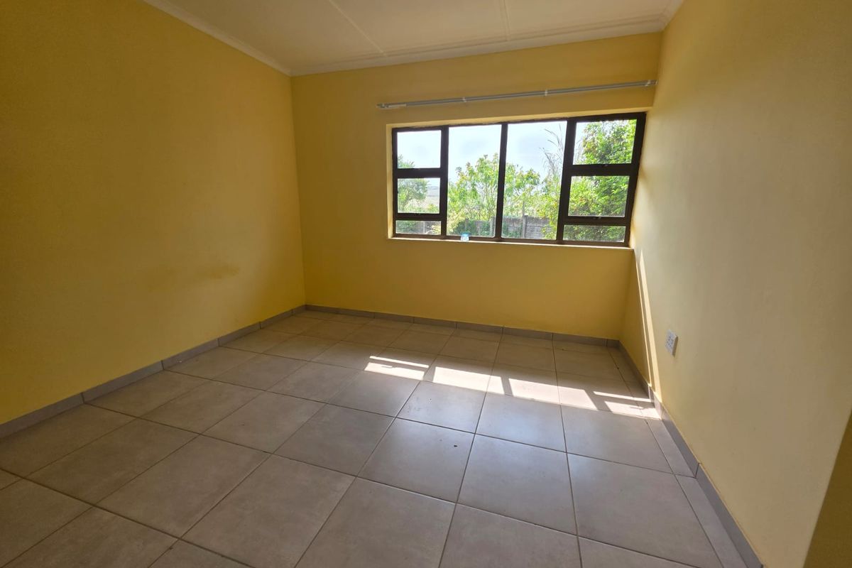A vacant bedroom featuring neutral tiled flooring, yellow painted walls, and large aluminium-framed windows allowing for natural light.