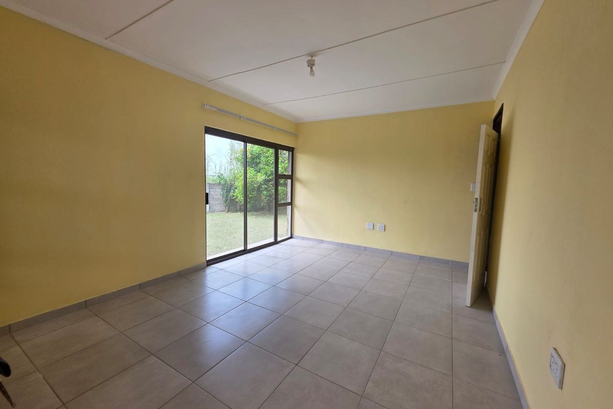 An empty living room featuring neutral tiled flooring, yellow walls, and a sliding glass door providing access to the rear garden.