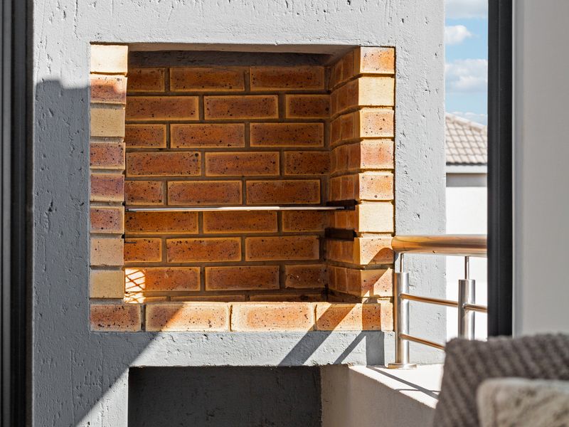 A modern balcony featuring a built-in brick braai and a sleek stainless steel railing, offering a clean and functional outdoor entertainment space.