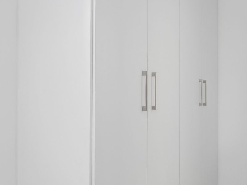 A clean and modern bedroom featuring floor-to-ceiling built-in cupboards with minimalist handles and neutral tiled flooring.