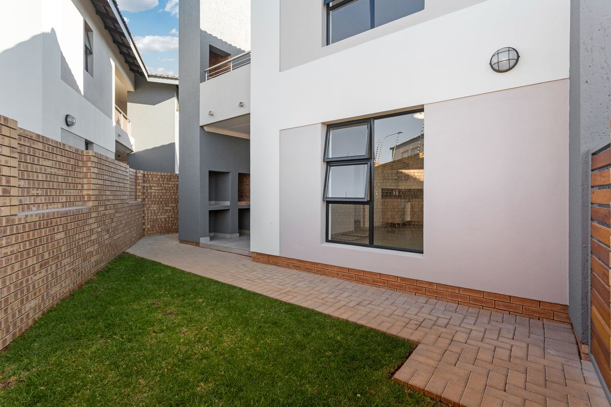 A well-maintained rear exterior area featuring a paved walkway, small lawn, brick boundary wall, and a built-in braai area.