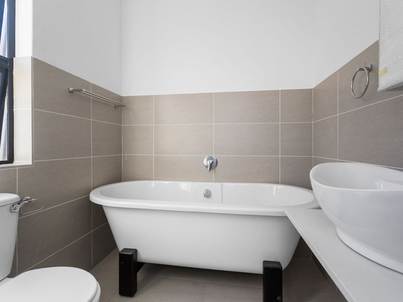 Modern bathroom featuring a freestanding bathtub, vessel sink with wall-mounted faucet, and neutral-toned wall and floor tiling.