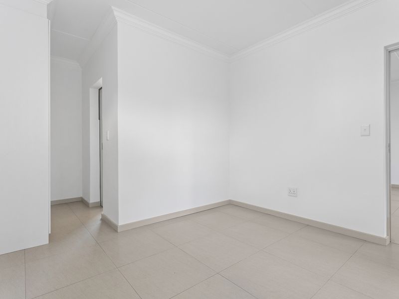 A bright, empty living area featuring neutral tiled flooring, clean white walls, and classic coving, offering a versatile blank canvas for interior design.