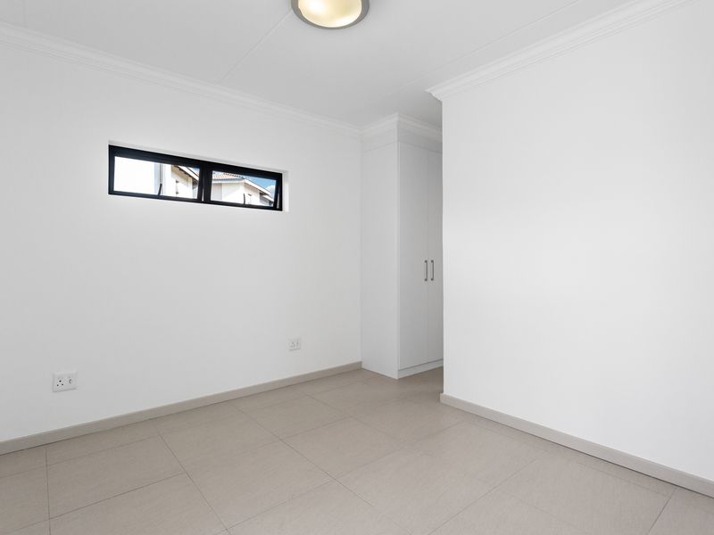 A clean, bright, and empty bedroom featuring neutral tiled flooring, built-in storage, and a modern clerestory window.