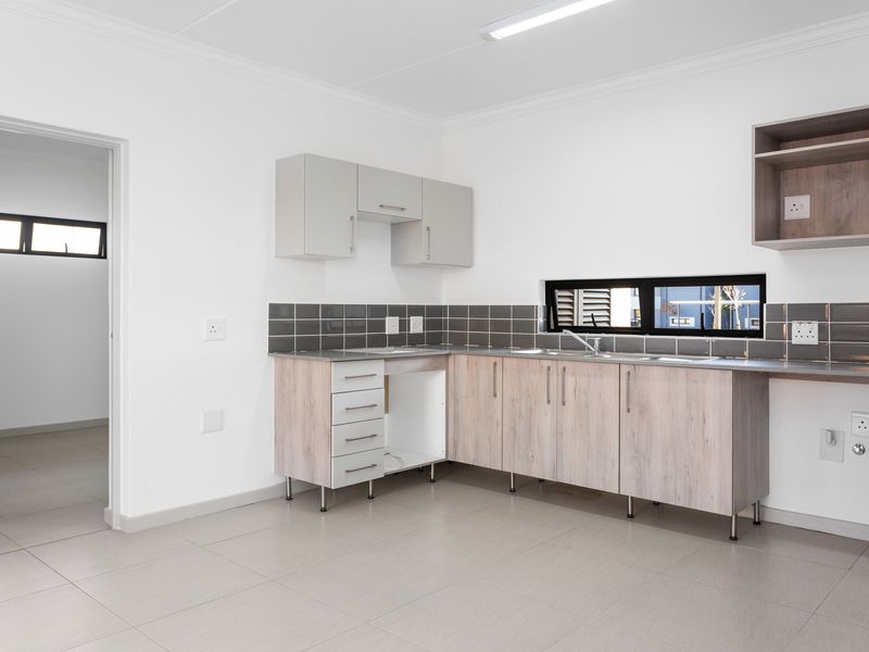 A clean, modern kitchen featuring light wood-tone cabinetry, a tiled backsplash, and neutral floor tiles, offering a functional and bright workspace.