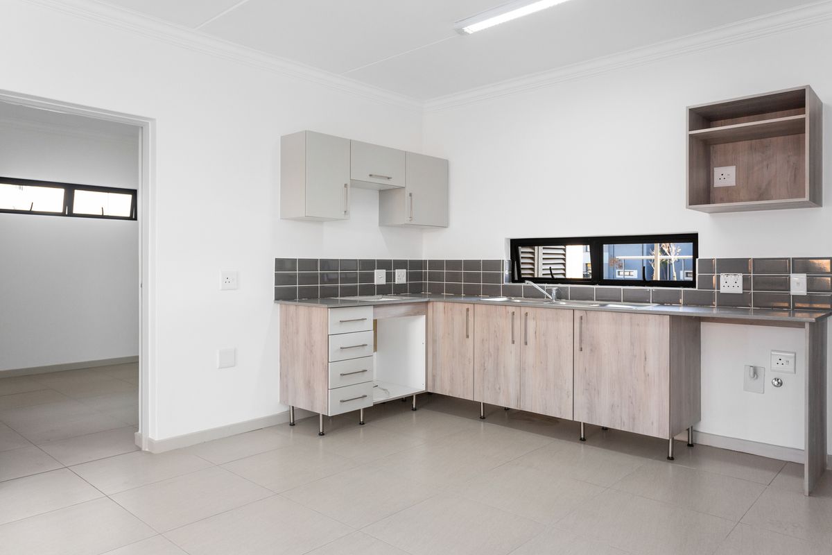 A clean, modern kitchen featuring light wood-tone cabinetry, a tiled backsplash, and neutral floor tiles, offering a functional and bright workspace.
