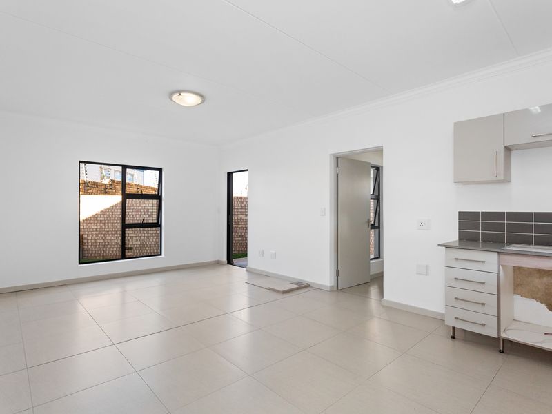 An open-plan living and kitchen area featuring neutral tiled flooring, modern aluminium windows, and a partially fitted kitchen with backsplash tiling.