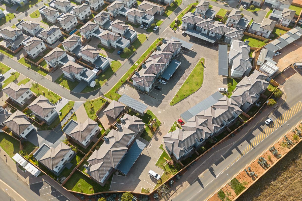 An aerial view of a modern residential apartment complex featuring tiled roof units, paved driveways, carports, and well-maintained communal garden areas.