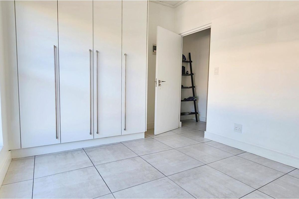 A bright bedroom featuring neutral floor tiles and extensive built-in floor-to-ceiling cabinetry with modern handles.
