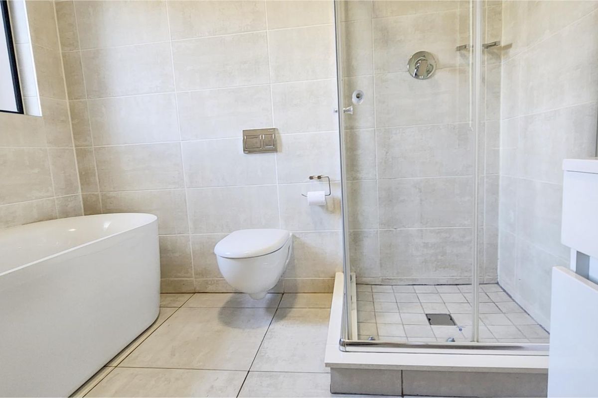 Modern bathroom featuring a freestanding bathtub, a glass-enclosed shower, and a wall-mounted toilet with neutral floor-to-ceiling tiling.