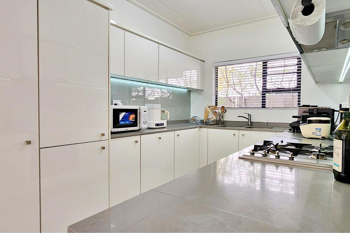 Modern kitchen featuring sleek white cabinetry, stone countertops, a built-in gas hob, and an integrated extractor fan with under-cabinet lighting.