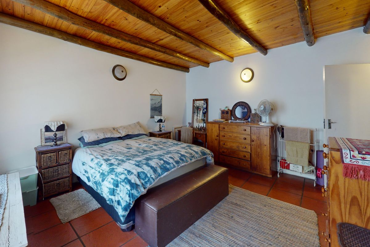 A bedroom featuring a rustic exposed timber beam ceiling and traditional terracotta floor tiles, offering a warm and characterful living space.