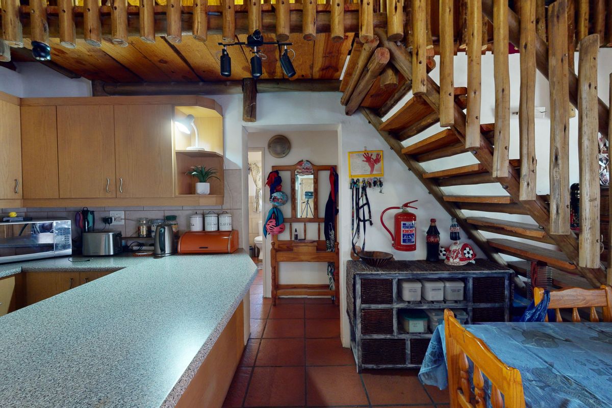A rustic kitchen featuring laminate cabinetry and countertops, tiled flooring, and an open timber staircase leading to an upper level.