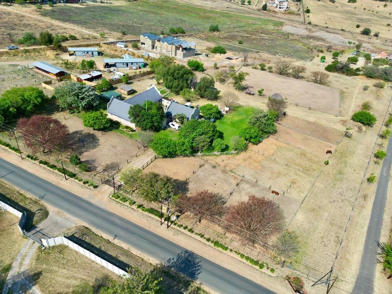 Aerial view of a large rural property featuring a main residence, multiple outbuildings, fenced paddocks, and established trees on a spacious plot.