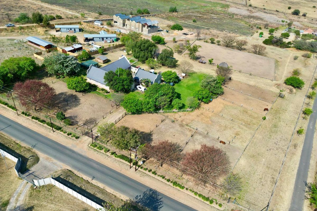 Aerial view of a large rural property featuring a main residence, multiple outbuildings, fenced paddocks, and established trees on a spacious plot.