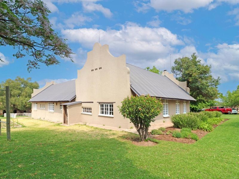 A well-maintained house featuring traditional Cape Dutch gables, a corrugated metal roof, and established garden surroundings.
