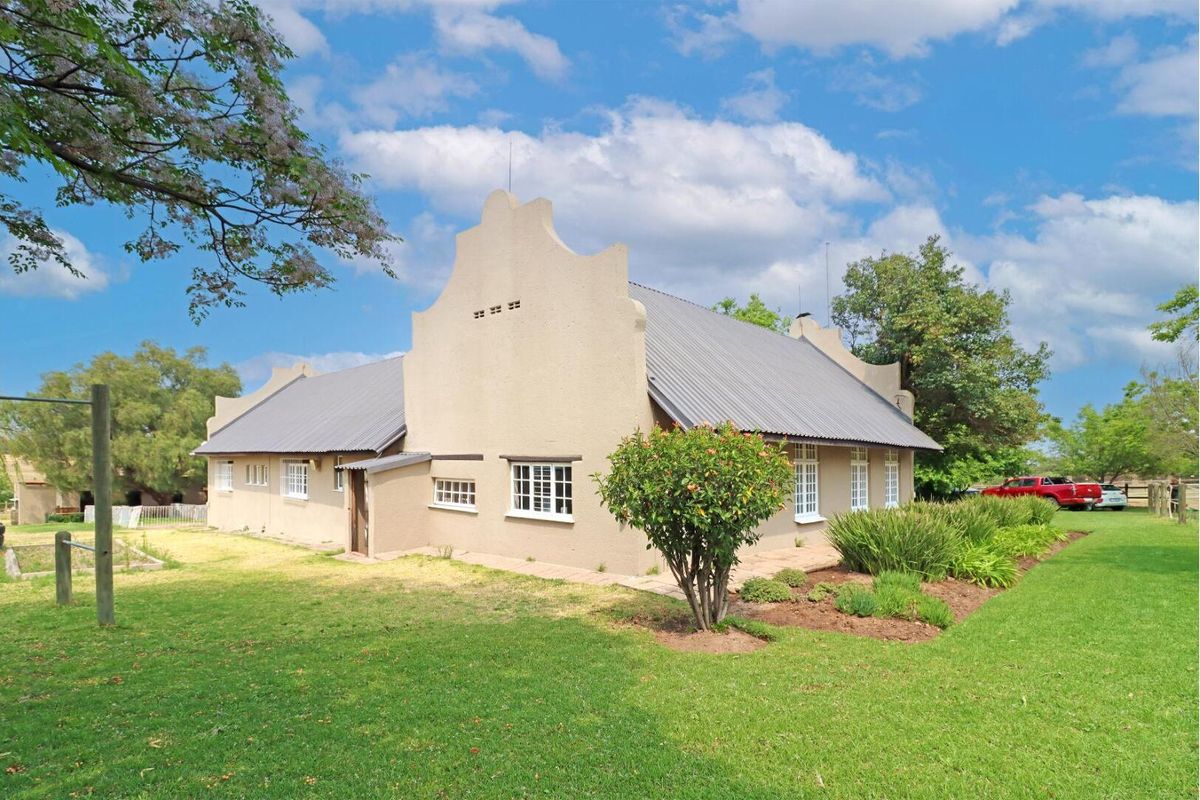 A well-maintained house featuring traditional Cape Dutch gables, a corrugated metal roof, and established garden surroundings.