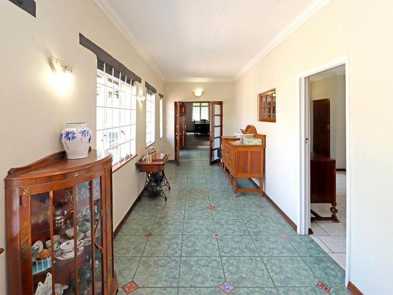 A spacious hallway featuring decorative tiled flooring, classic cornicing, and timber-framed glass doors leading to adjacent living areas.