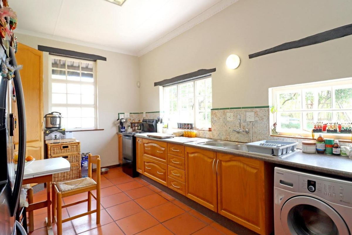A functional kitchen featuring wooden cabinetry, laminate countertops, a double basin sink, and terracotta floor tiles with ample natural light from multiple windows.