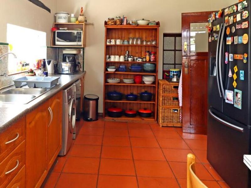 A functional kitchen featuring timber cabinetry, laminate countertops, a double bowl sink, and terracotta-style tiled flooring.