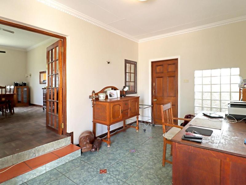A functional home office space featuring tiled flooring, a glass block window, and timber french doors leading into an adjacent dining area.