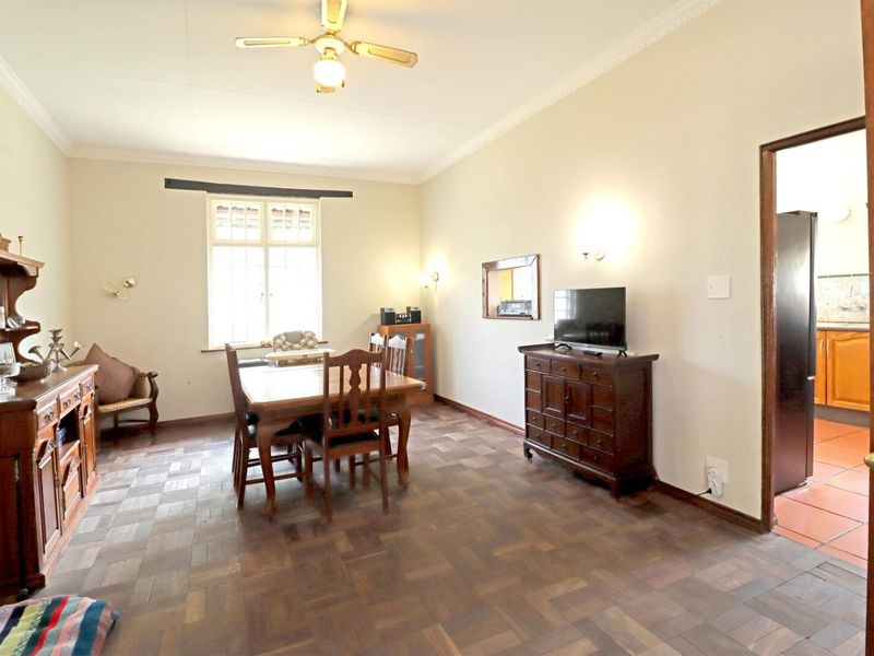 A spacious dining room featuring classic parquet flooring, coved cornicing, and a ceiling fan, with direct access to the adjacent kitchen area.