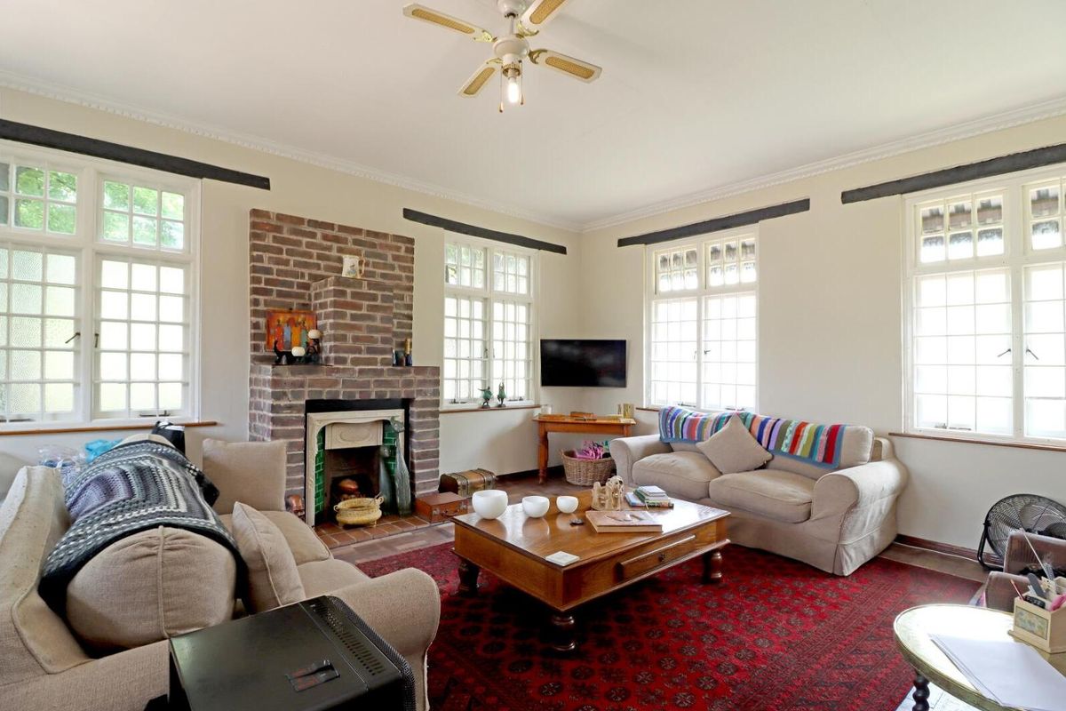 A spacious living room featuring a classic brick fireplace, ceiling fan, and large multi-pane windows that provide ample natural light.