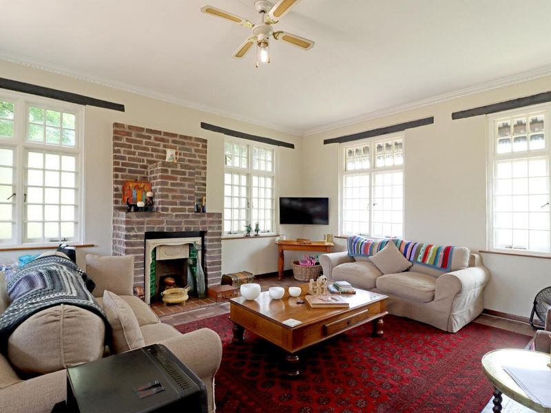 A spacious living room featuring a classic brick fireplace, ceiling fan, and large multi-pane windows that provide ample natural light.