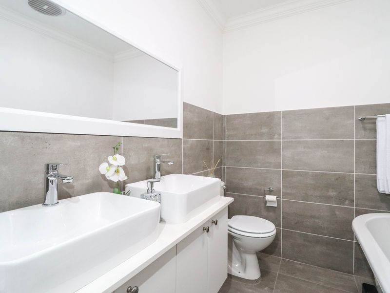Modern bathroom featuring a double vanity with vessel sinks, chrome fixtures, a freestanding bathtub, and neutral grey wall and floor tiling.