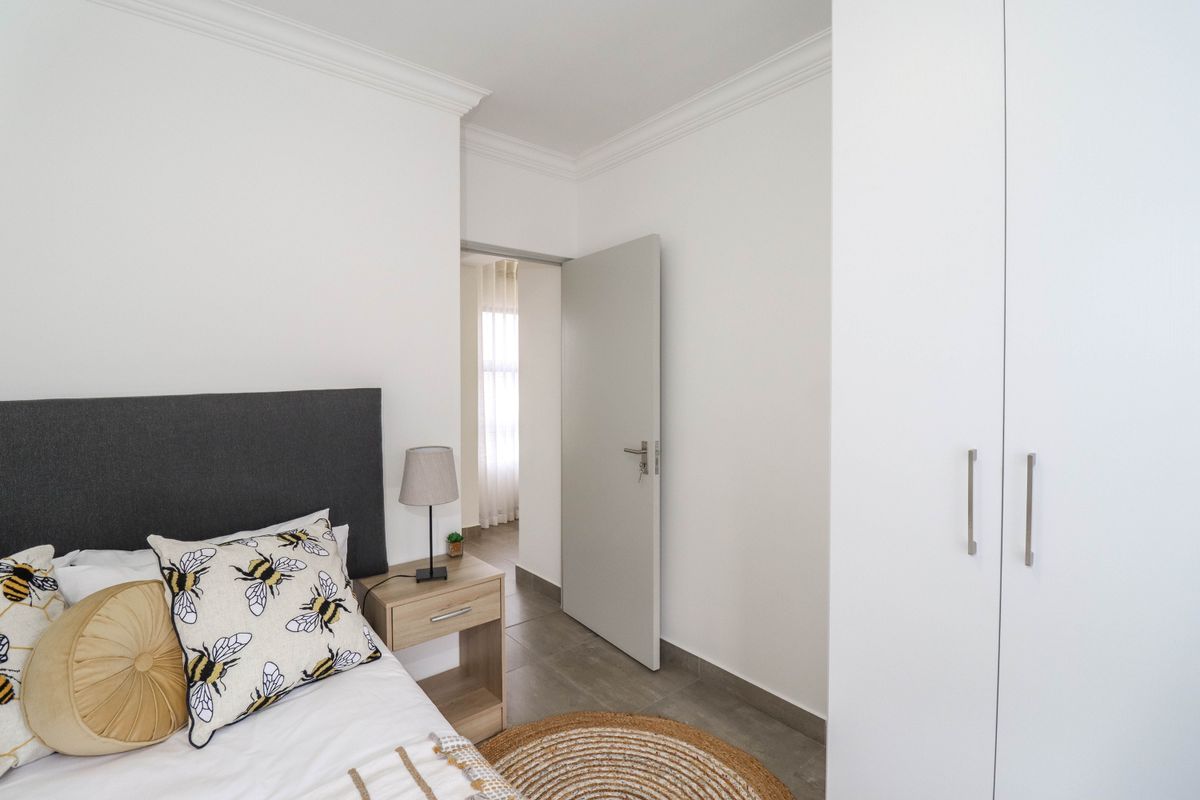 A well-maintained bedroom featuring neutral tiled flooring, crisp white walls, decorative ceiling cornicing, and a modern built-in wardrobe.