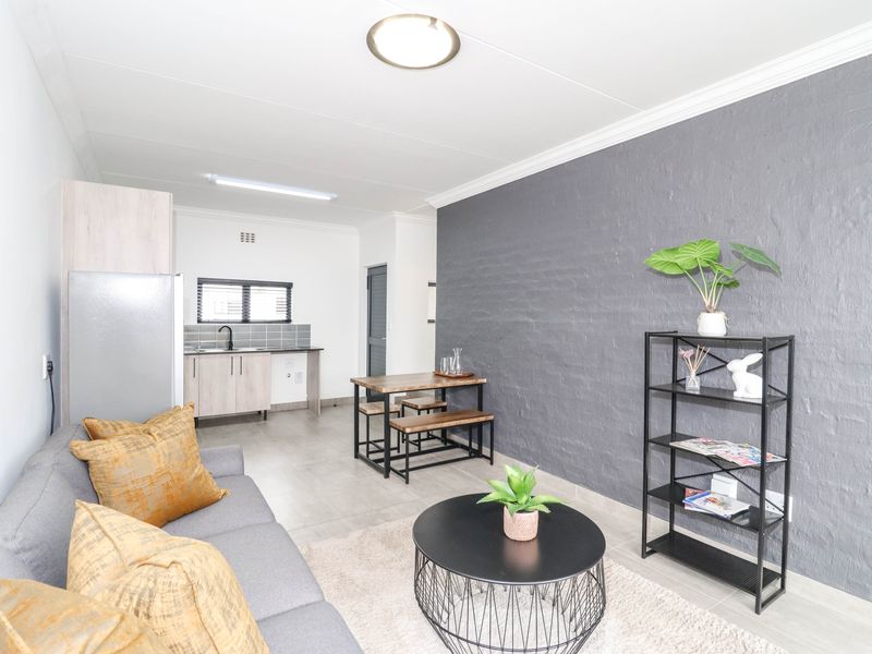Open-plan living area featuring a modern kitchen corner with cabinetry, tiled flooring, and a striking grey textured feature wall.
