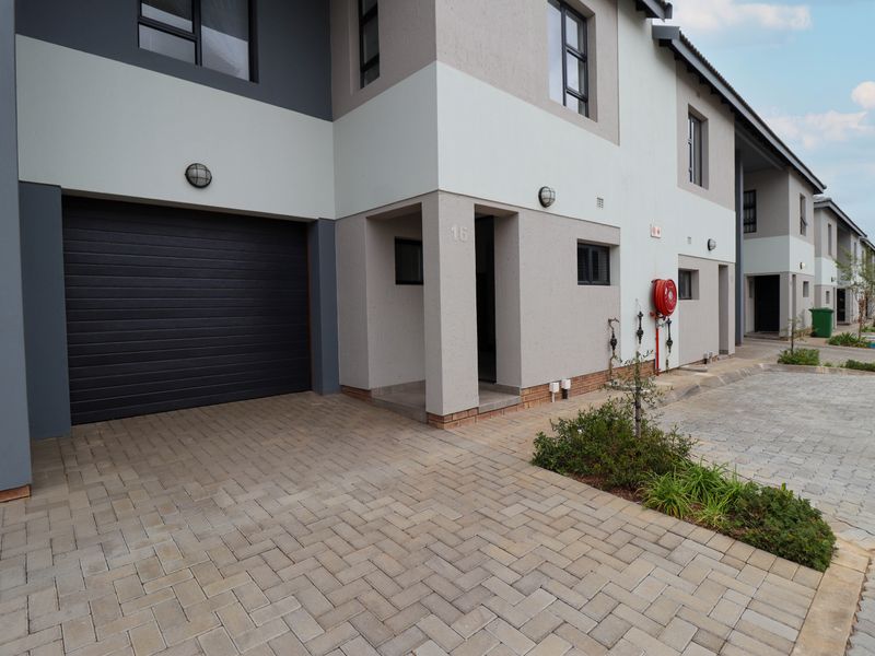 Modern townhouse exterior featuring a paved driveway, automated garage door, and clean architectural lines with contemporary finishes.