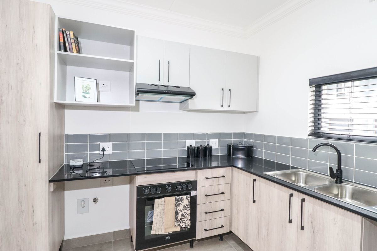 Modern kitchen featuring light wood-grain cabinetry, black granite countertops, a built-in oven with hob, extractor fan, and a stainless steel double sink.