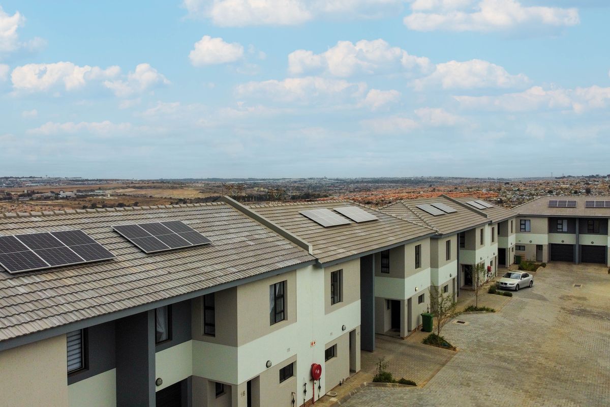 Aerial view of a townhouse complex featuring modern tiled roofs with installed solar panels and a paved communal driveway area.