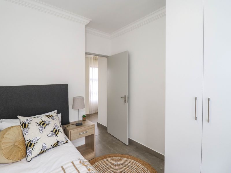 A well-maintained bedroom featuring neutral tiled flooring, crisp white walls, decorative ceiling cornicing, and a modern built-in wardrobe.
