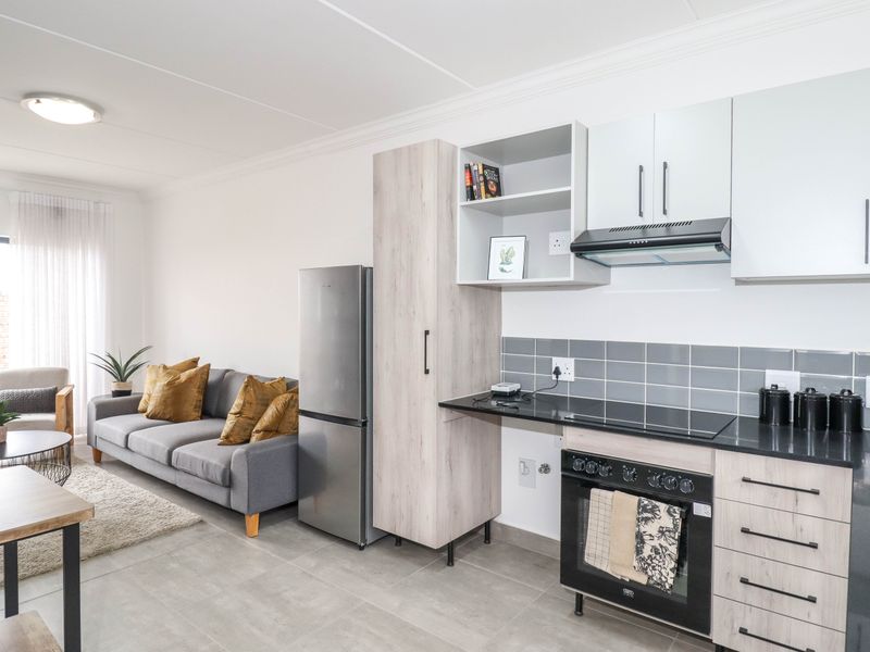 Modern open-plan living area featuring a well-appointed kitchen with built-in cabinetry, electric oven, hob, and tiled flooring, seamlessly flowing into the lounge space.