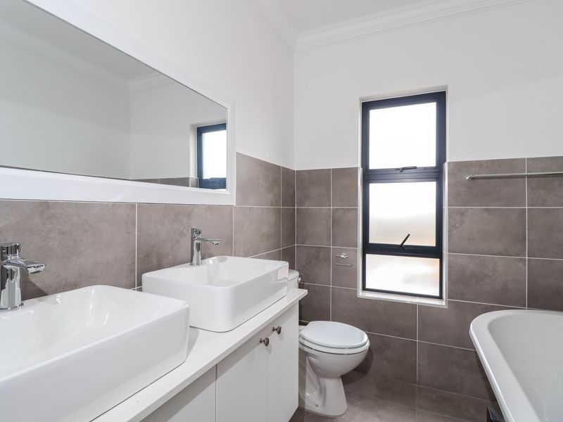 Modern bathroom featuring a double vanity with vessel sinks, a bathtub, and neutral-toned wall and floor tiling.