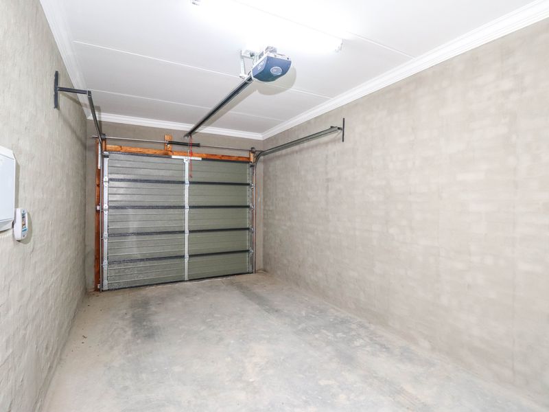 A clean, empty single-car garage featuring a sectional door with an automatic opener, concrete flooring, and unpainted masonry walls.