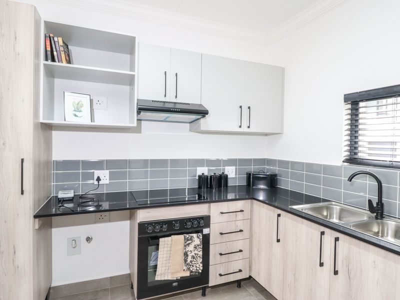 Modern kitchen featuring light wood-grain cabinetry, black granite countertops, a built-in oven with hob, extractor fan, and a stainless steel double sink.